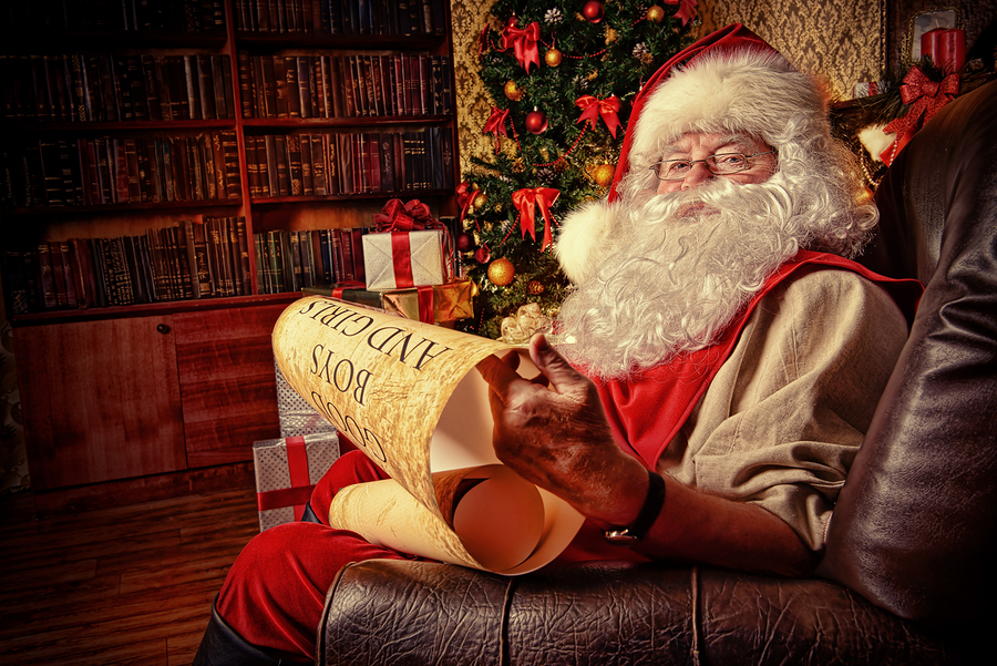 Santa Claus dressed in his home clothes sitting in the room by the fireplace and Christmas tree. He is reading a list of good boys and girls. Christmas. Decoration.